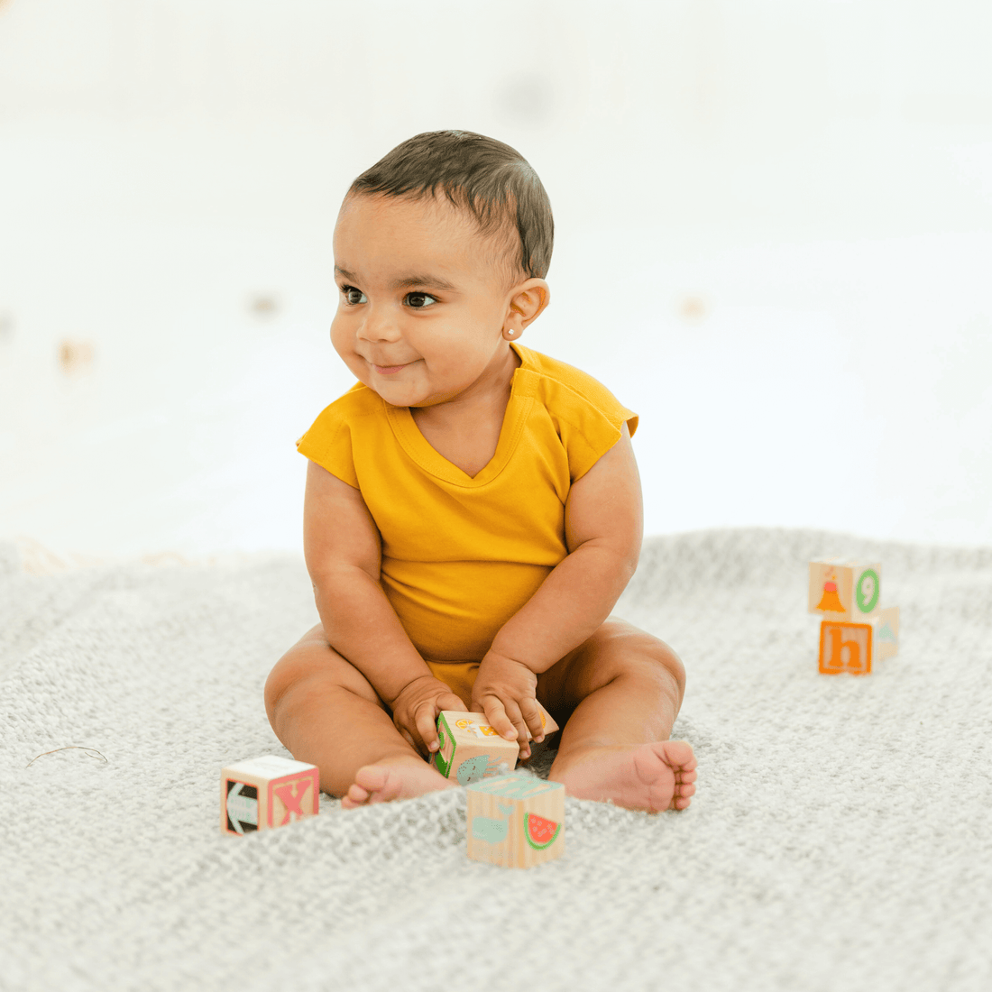 happy-baby-wearing-a-yellow-onesie,-sitting-on-a-blanket-with-colorful-blocks,-showcasing-comfort-and-playfulness.