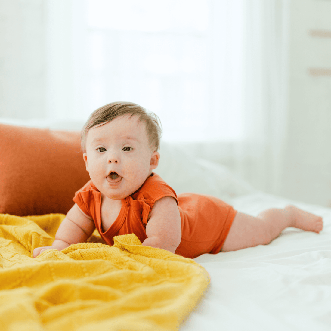 baby-in-an-orange-onesie-on-a-bed,-showcasing-the-comfort-and-ease-of-dressing-with-our-bottom-up-bodysuit.