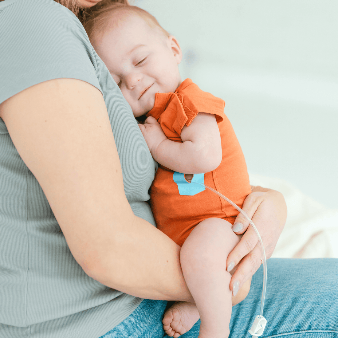 baby-comfortably-snuggled-in-an-orange-onesie-with-a-tube-eeze-iron-on-patch,-sharing-a-moment-with-parent.