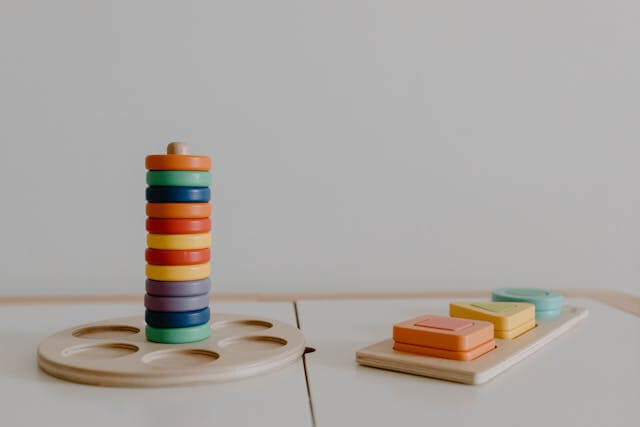 Colorful wooden stacking toy beside shape sorting blocks, promoting sensory play in childhood development.
