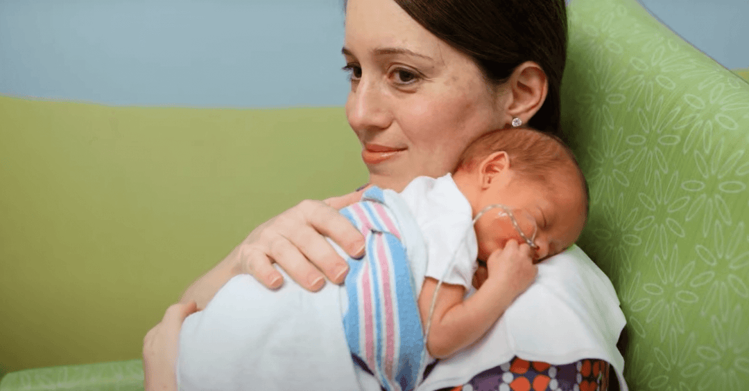 Mother holding her premature baby in the NICU, showcasing love and support during a challenging time.