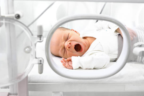 Newborn baby yawning in a NICU incubator, showcasing healthcare and nurturing environment.