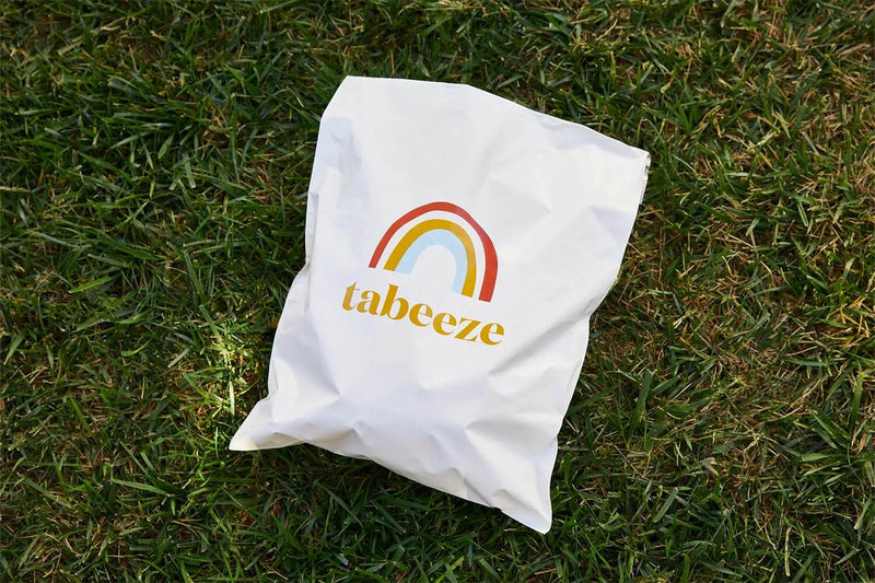White bag with tabeeze logo and rainbow design on grass.