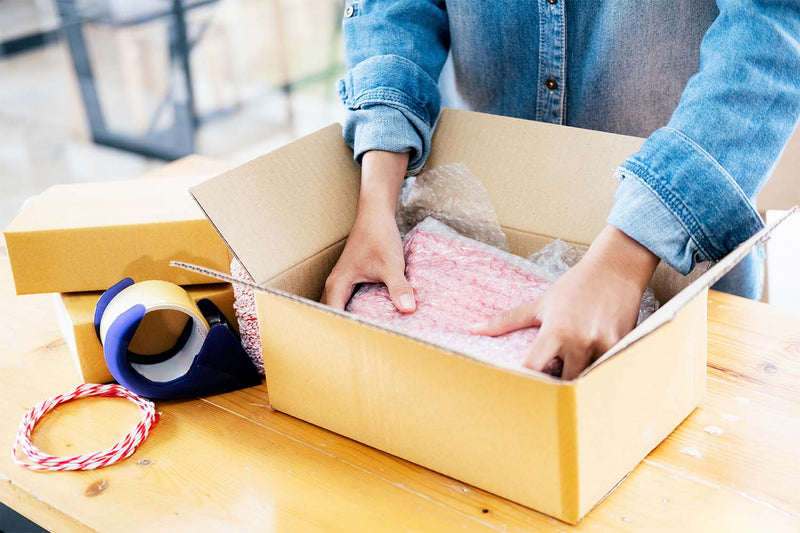 Person packing eco-friendly baby shower gifts in a cardboard box with cushioning material.
